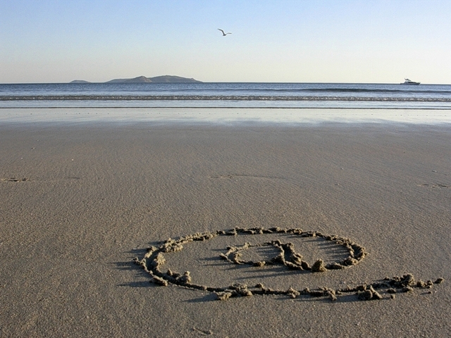 fotografie písečné pláže, v dálce moře, na písku nakreslený zavináč